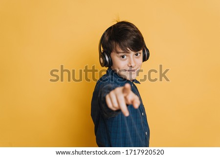 Young pretty boy in headphones, dressed in casual shirt, cute smiling, pointing at you over yellow backdrop. Make your choose.
