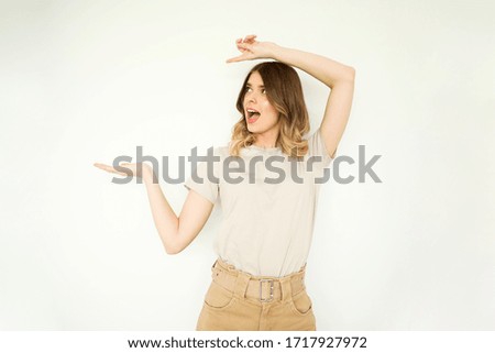 Photo of surprised young woman standing isolated over white wall background. Pointing to copy space, neutral palette. 