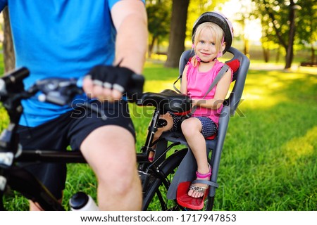 child a little girl in a Bicycle helmet smiles sitting in a child's Bicycle seat against the background of a Park and green grass. Royalty-Free Stock Photo #1717947853