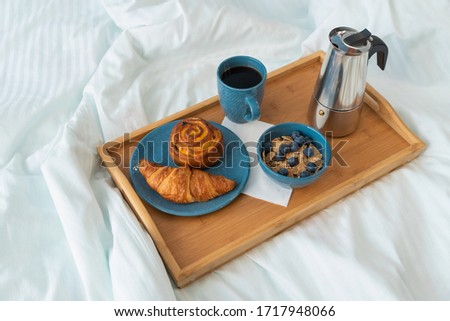 Breakfast served in bed on wooden tray with coffee and croissants. Concept of good morning