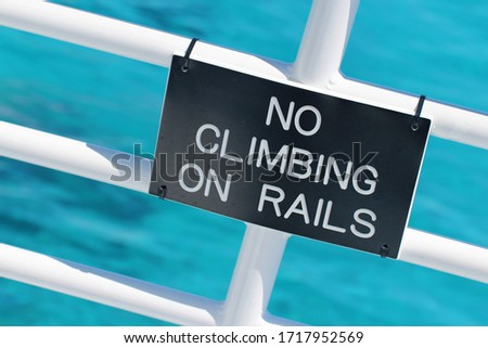 Warning sign on a white ship's rail, blue-green water in soft-focus in the background.