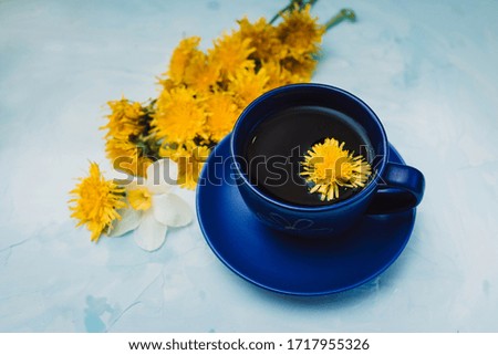 Dark blue cuptea over blue background decorated with yellow dandelions flowers. Stay at home. Good morning concept