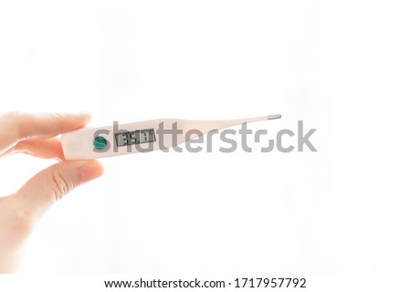 The fingers of a female hand hold an electronic thermometer with a temperature of 35.7 degrees on a scoreboard on a white background. Pathology, disease, hypothermia. Royalty-Free Stock Photo #1717957792