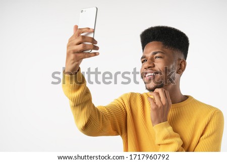 Portrait of young african american man using smartphone to take selfie pictures and smiling standing against white background