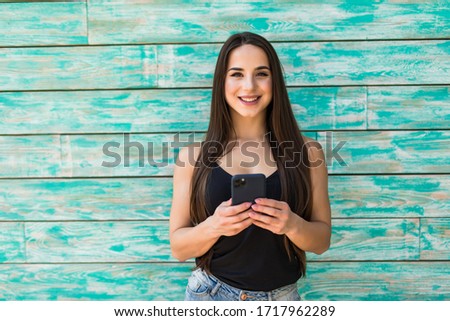 Young woman typing phone while standing outdoors on gray background