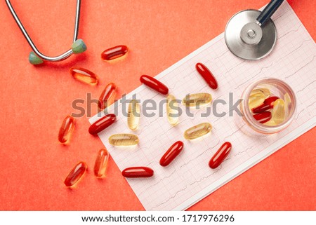 Vitamins in capsules Omega 3, D3, stethoscope and cardiogram on the table. Top view. Orange background.