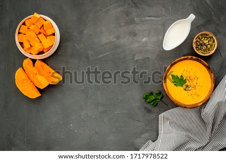 Pumpkin soup on grey table top view. Ingredients in bowls. Copy space