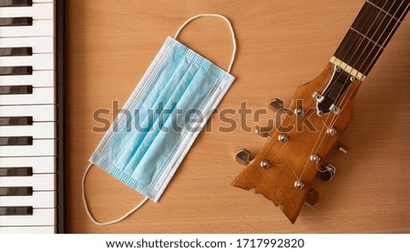 Piano keys, acoustic guitar and blue medical mask lie on a wooden background. Coronavirus epidemic music concept