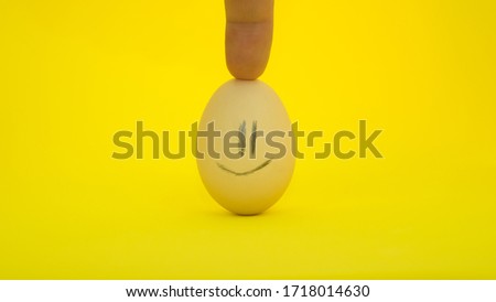 Egg with a smile,cheerful with mood, bright background,finger holds the egg in an upright position.Egg with emotions,close-up.