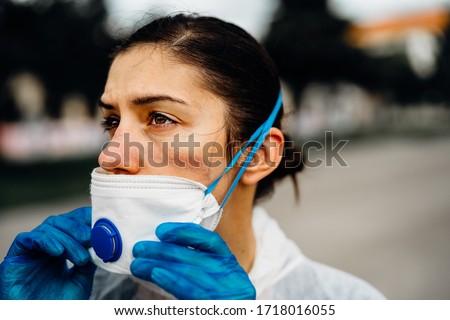 Exhausted doctor/nurse wearing coronavirus protective gear N95 mask uniform.Coronavirus Covid-19 outbreak.Mental stress of frontline worker.Face scars.Mask shortage.Overworked healthcare professional Royalty-Free Stock Photo #1718016055