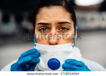 Exhausted doctor/nurse wearing coronavirus protective gear N95 mask uniform.Coronavirus Covid-19 outbreak.Mental stress of frontline worker.Face scars.Mask shortage.Overworked healthcare professional Royalty-Free Stock Photo #1718016064