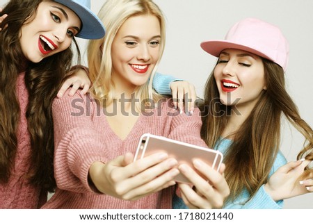 Three happy best girlfriends wearing sweaters and caps making selfie