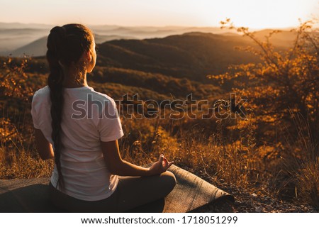Woman meditating alone on hill with amazing autumn mountain view at sunset. Zen spiritual concept. Praying alone, harmony with nature.