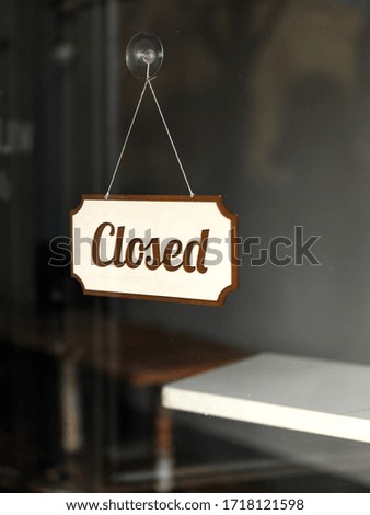 "Closed" written on a signed hanging on the window of a coffee due to COVID-19 social distancing and stay at home rules, with small surface of white bench exposed. 