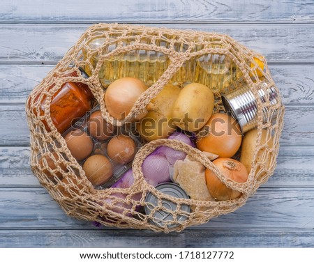 Close up of eco-friendly string, mesh reusable net bag with canned food, eggs, vegetables, oil and garlic. Crisis stock of shelf stable food. Quarantine, isolation period. Safe home delivery.