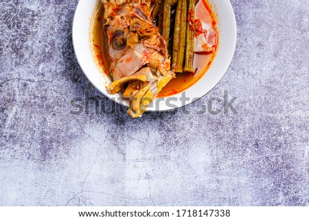 A flatlay picture part of red snapper head in "asam pedas" on copy space crack background.  "Asam pedas" is sour soup made from tamarind, chilli and spices that is popular in Malaysia and Indonesia.