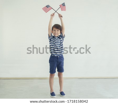 Portrait of a caucasian little boy holding and waving american flag in his two hands to celebrate independence day on 4th of July. Independence Day of USA concept