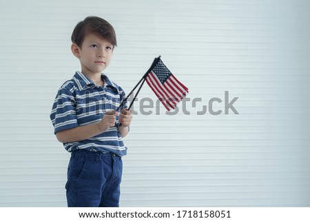 Portrait of a caucasian little boy holding and waving american flag in his two hands to celebrate independence day on 4th of July. Independence Day of USA concept