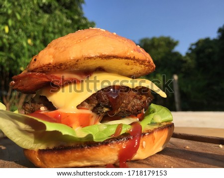 Close-up photo of home made hamburger with beef, onion, tomato, lettuce, cheese and spices. Fresh burger closeup on wooden rustic table with potato fries and chips.
