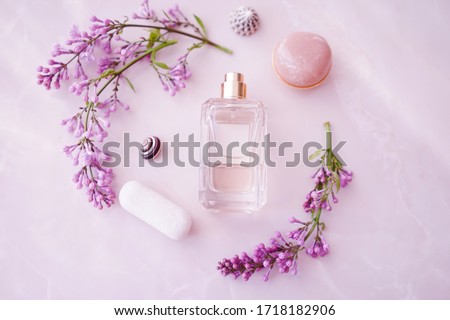     glass perfume bottle with delicate lilac flowers on a textured surface lit by the sun. Top  view                            Royalty-Free Stock Photo #1718182906