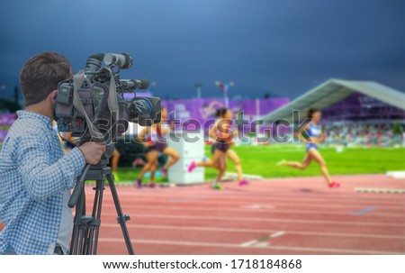 Cameraman shooting live broadcast from athletics game to television and internet on the background blured Unidentified women athletes 