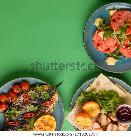 Holiday celebration table setting with food. Flat-lay of sweet cheesecake, fruit salad, meat dishes. Top view of different meals over bright green background. Copy space banner. Frame picture.
