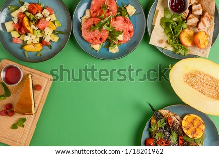 Holiday celebration table setting with food. Flat-lay of sweet cheesecake, fruit salad, meat dishes. Top view of different meals over bright green background. Copy space banner. Frame picture.