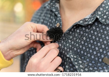Sound engineer fastens lavalier microphone on actor's clothes for interview