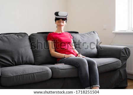 Young woman with VR set sitting on the couch in living room at home. VIrtual reality travel, shopping, learning