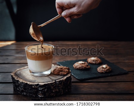Homemade creamy Dalgona coffee along with some homemade cookies. Hand serving coffee with a spoon. Dark photography.