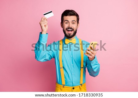 Portrait of his he nice attractive cheerful cheery glad excited lucky bearded guy wearing mint blue shirt holding in hands cell bank card lottery winner isolated over pastel pink color background