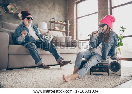 Photo of two people grandparent little granddaughter cool vintage style specs denim outfit hat house party sit on tape player recorder sing mic old fashion song stay home quarantine indoors