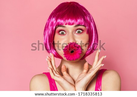 Image of amusing beautiful woman in wig posing with flower in her mouth isolated over pink background