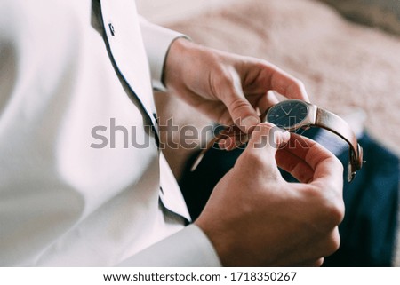 the groom in a white shirt holds his watch in his hands