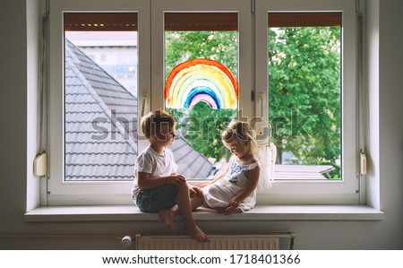 Cute little children on background of painting rainbow on window. Photo of kids leisure at home, safety joy symbol, happy childhood. Positive visual support during quarantine. Family Art Background