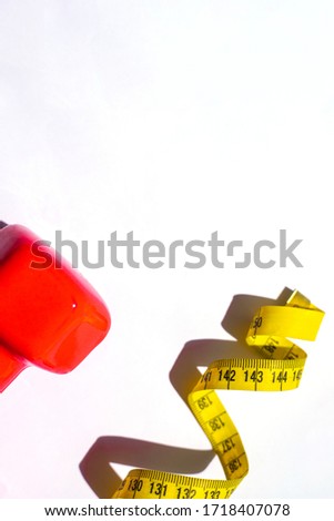 Red dumbbells and a centimeter-long yellow ribbon on a white background. Athletic activity.Fitness at home.Diet.