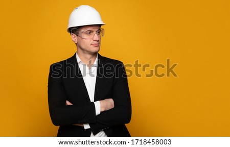 Serious business. Close-up photo of a young architect in formal outfit and hard hat, who is standing with folded arms and looking aside.
