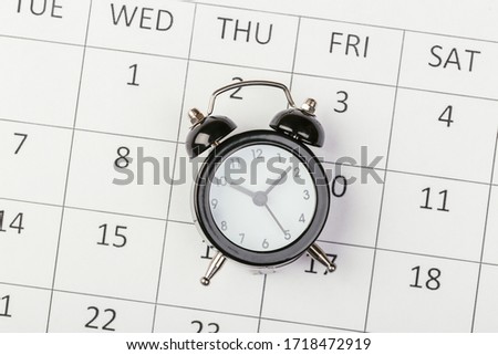 Flat lay or top view of black alarm clock with white calendar on wooden  board with copy space, schedule for vacation, reminder for business appointment or deadline for business project.