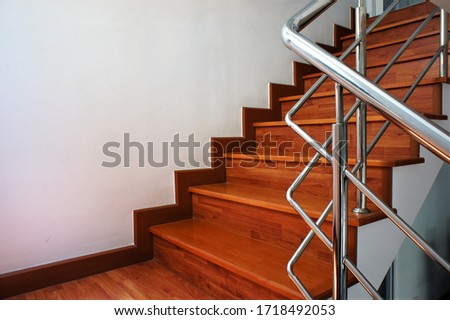  Selective focus on a stainless steel railing, which is installed on a wooden staircase beside a white cement wall.