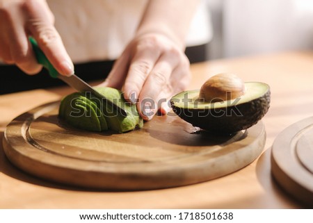 Close up of woman slicing avocado on wooden board at home. Vegetarian food concept Royalty-Free Stock Photo #1718501638