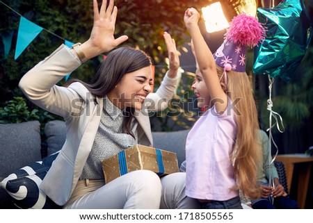 young adult female with arms up holding present for a little girl at birthday 