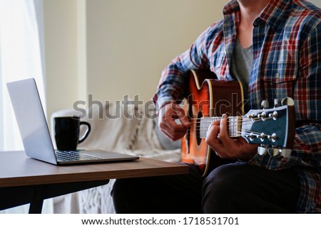 Music college hipster student practicing acoustic guitar exercise, reading notes from laptop computer. Man taking an online musical courses at home during quarantine. Background, close up