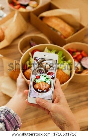 Female food blogger reviewing takeout food, taking video on phone. Italian sub sandwich, french croissant w/ salmon, chocolate cheesecake. Close up, top view, pov, copy space, wooden table background.