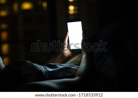 Girl on the bed before falling asleep looks at a smartphone. Check news and social networks before going to bed. Smart gadget. Royalty-Free Stock Photo #1718533912