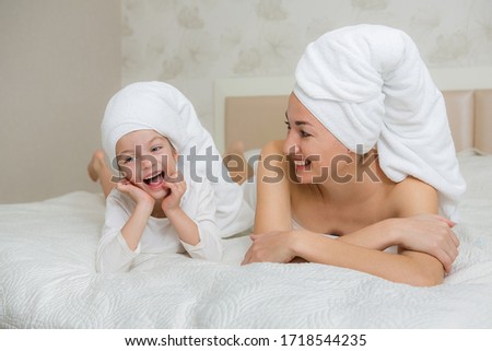 Mother and her daughter playing and hugging in the bed. Little girl with mom in towel. Happy loving family. Beautiful young woman being kissed by a cute little girl. Happy mother's day.