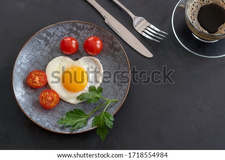 Breakfast with fried eggs, tomatoes and a cup of coffee. Fork and knife on a black background. Copy space. Royalty-Free Stock Photo #1718554984
