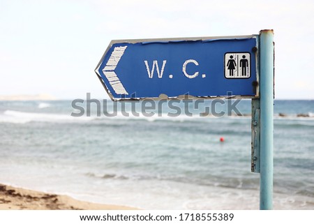 direction to the toilet on the beach. WC - inscription on signboard toilet hanging on a pole, a sea and sky background.