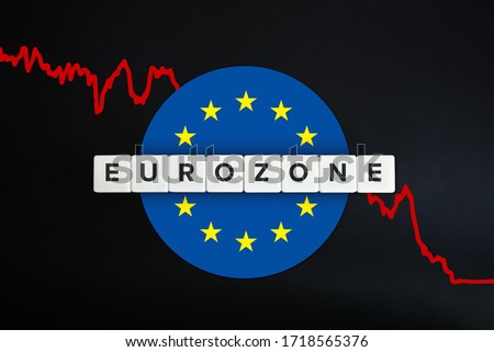 Eurozone or the euro area facing economic recession and decline of economy due to coronavirus or covid-19 crisis. European union (EU) flag, red stock chart and block letters on black background. Royalty-Free Stock Photo #1718565376