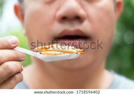 Food Insects: Man eating bamboo worm insect on spoon. Bamboo Caterpillar is good source of protein edible and delicious for future. Entomophagy concept. Royalty-Free Stock Photo #1718596402
