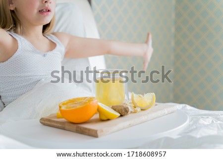 Little sick girl in bed with cup of antipyretic drugs for colds,flu.Tea with citrus vitamin C,ginger root,lemon,orange.Wooden tray. Home self-treatment.Medical quarantine covid-19 coronavirus therapy.
